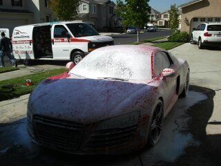 A car is covered in foam in a driveway next to a van
