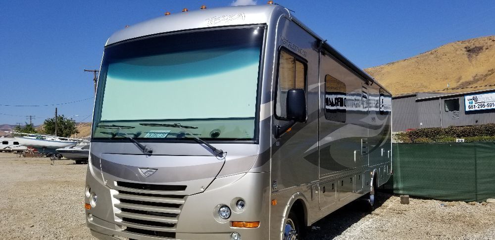 A large rv is parked in a gravel lot in front of a building.