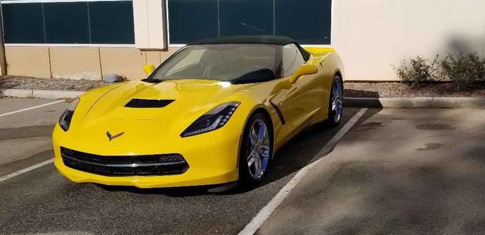 A yellow sports car is parked in a parking lot in front of a building.