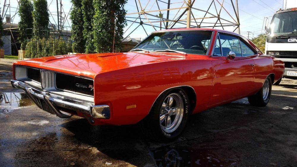 A red dodge charger is parked in a parking lot next to a truck.