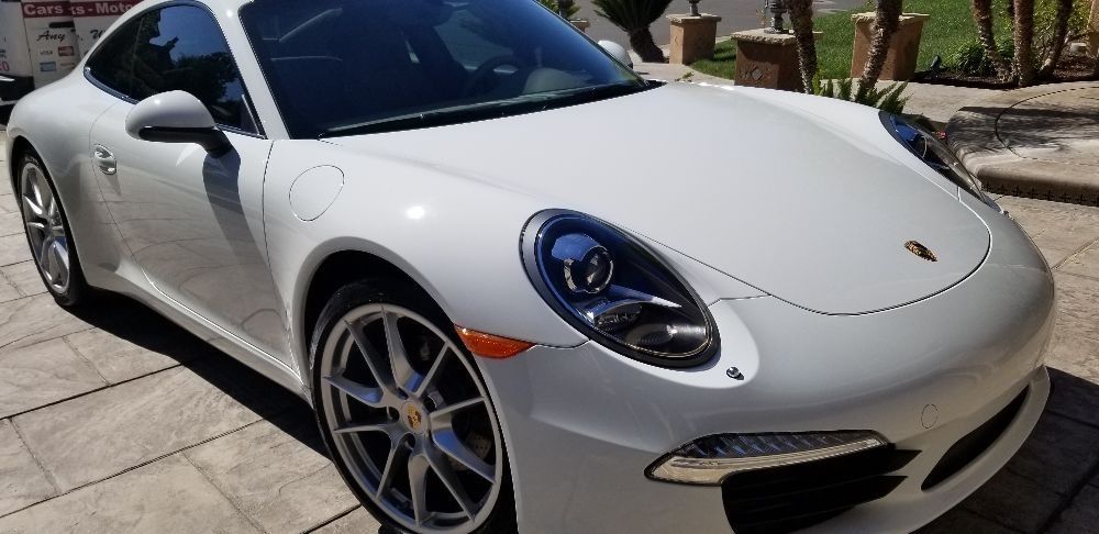 A white porsche 911 is parked on the side of the road.