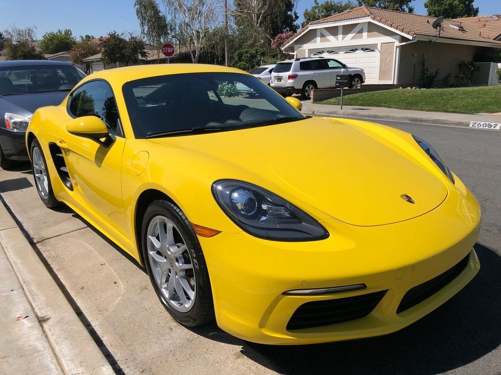 A yellow porsche boxster is parked on the side of the road.