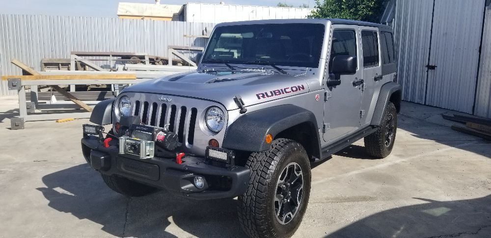 A silver jeep wrangler is parked in a parking lot.