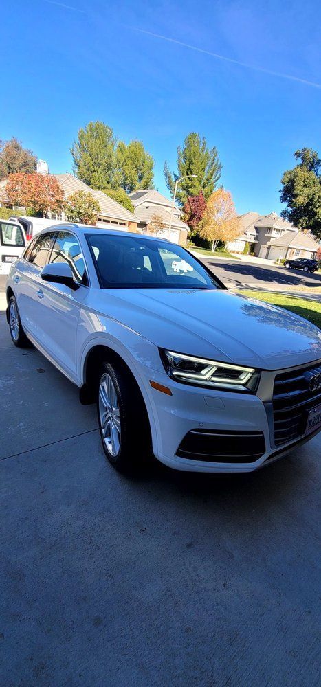 A white audi q5 is parked in a driveway on a sunny day.