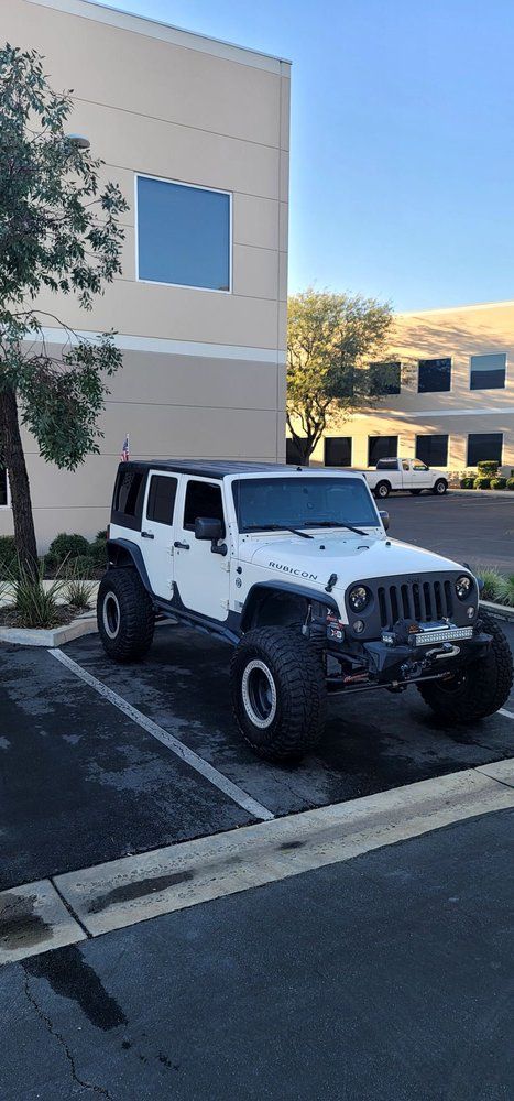 A white jeep is parked in a parking lot in front of a building.
