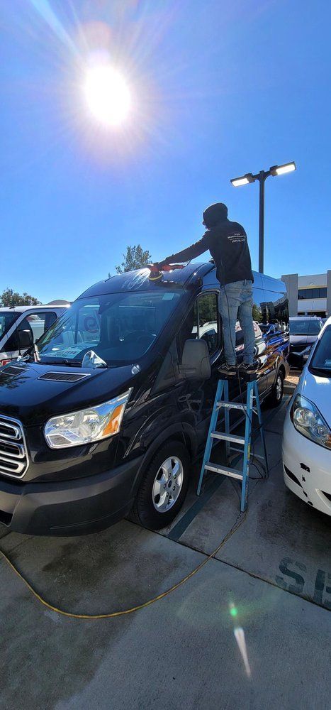 A man is standing on a ladder working on the roof of a van.