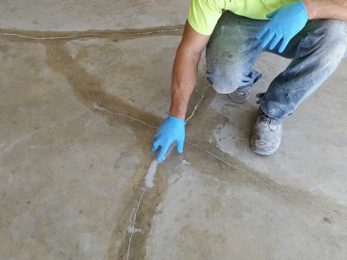 Person with blue gloves applying sealant to cracks in a concrete floor.