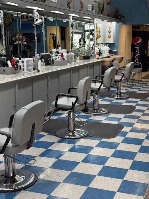 Hair salon interior with gray chairs, mirrors, and checkered blue and white floor.