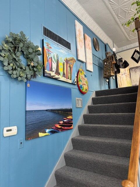 Blue-painted stairwell with gray carpeted steps, decorated with art and a wreath.