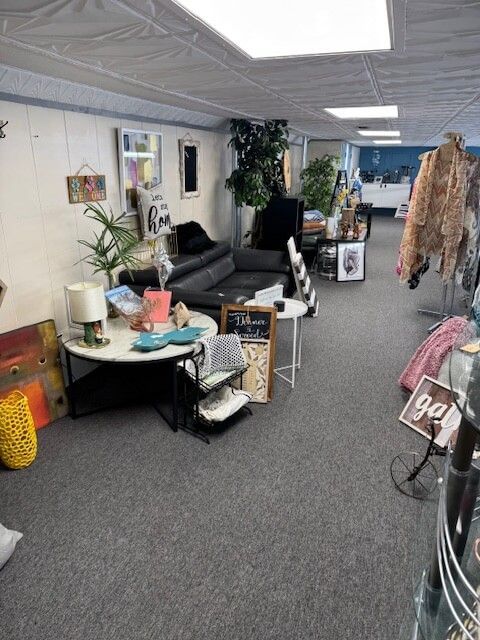 Interior of a store with furniture, decor, and clothing racks on display. Gray carpet, white walls.