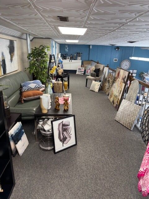 Interior with art, furniture, and décor. Green sofa, wall art leaning against wall, items on floor and tables.