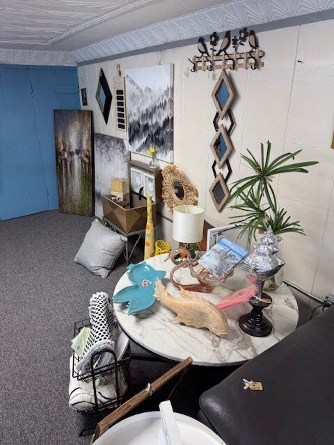 A cluttered room with artwork, a table with various objects, and a black bench.