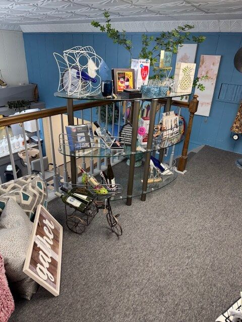Display table with decorative items in a shop, blue wall backdrop, gray carpet, and a staircase.