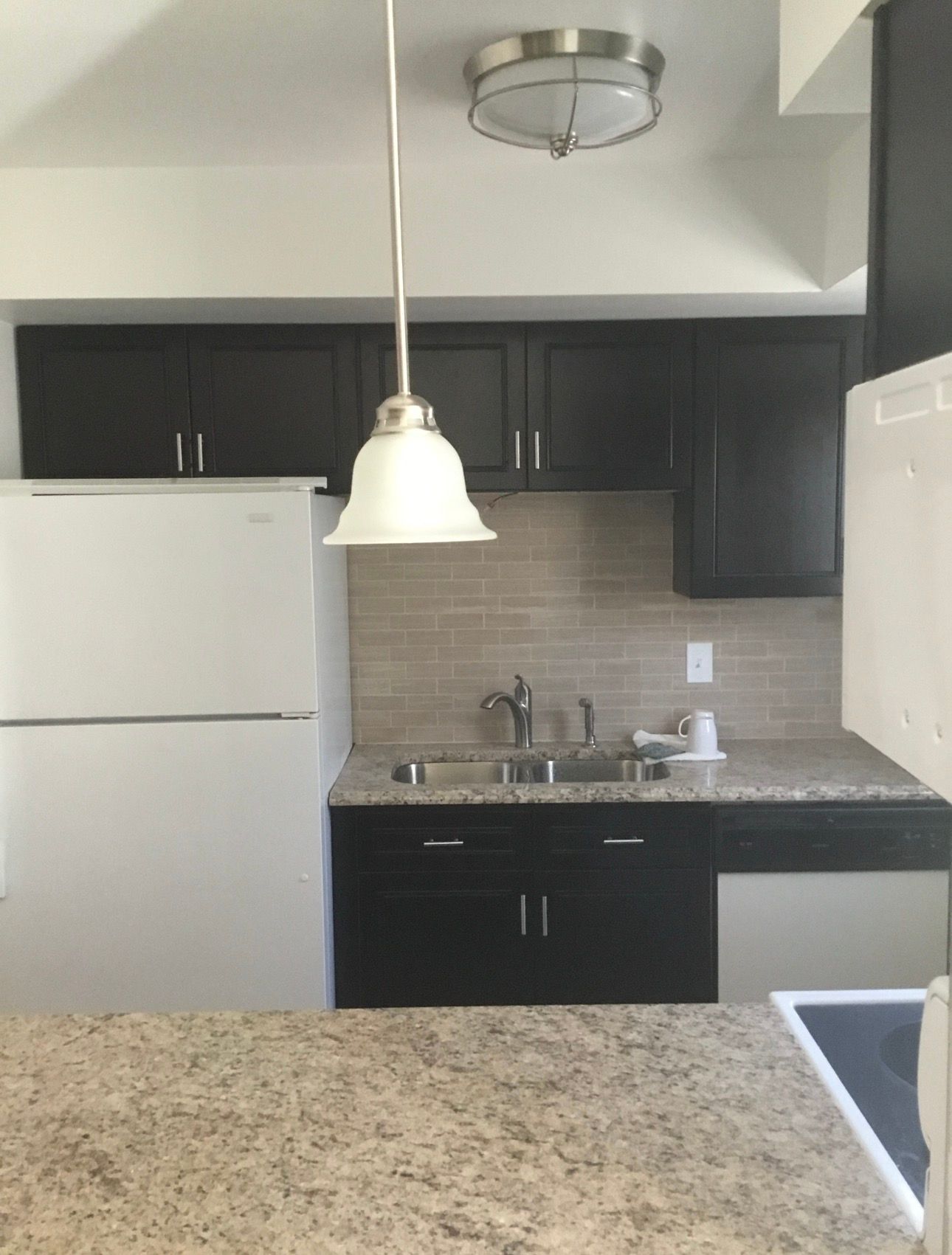 Kitchen with black cabinets, white appliances, and a hanging light.