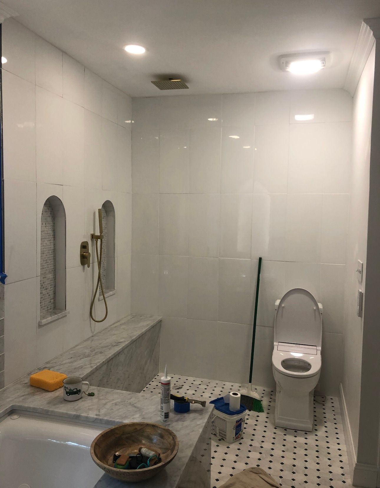 White bathroom with tiled walls, toilet, shower niche, and granite bench.