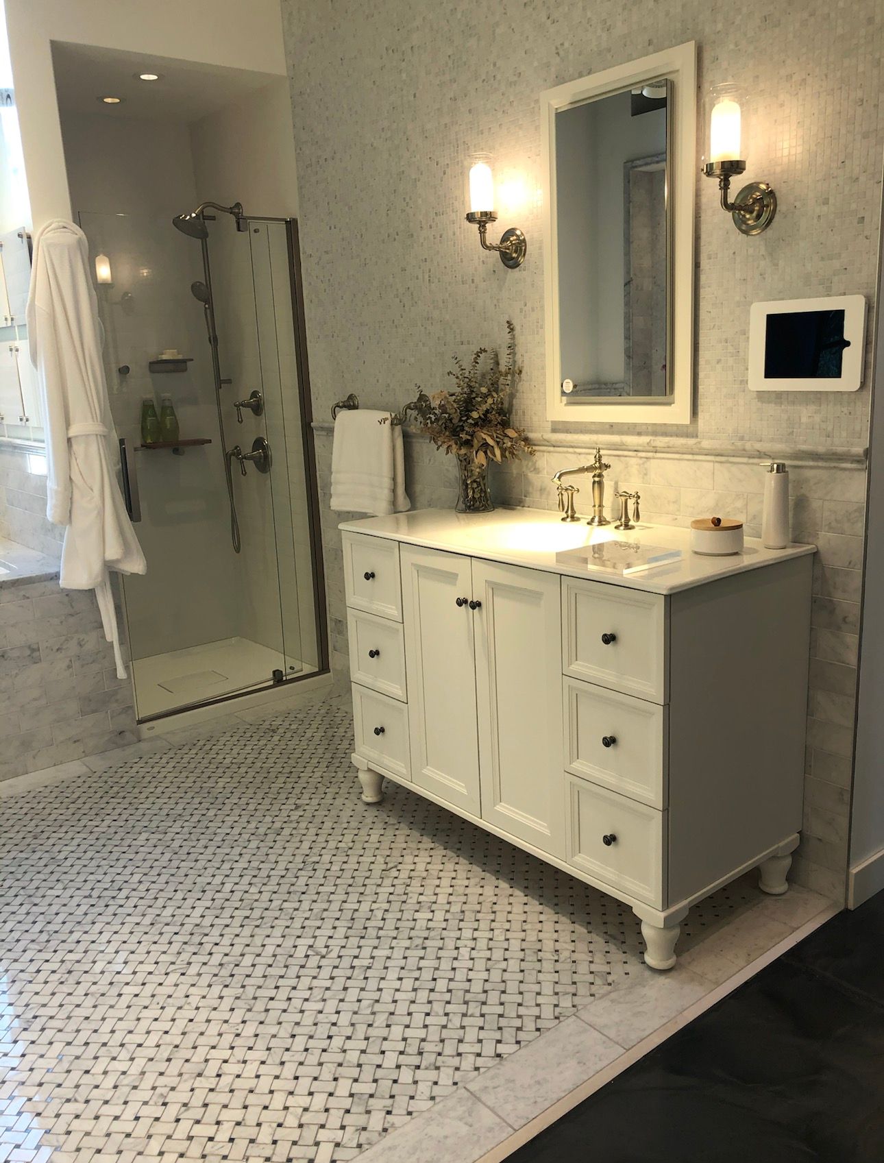 White bathroom with marble tiles, a white vanity with drawers, a shower, and a mirror.