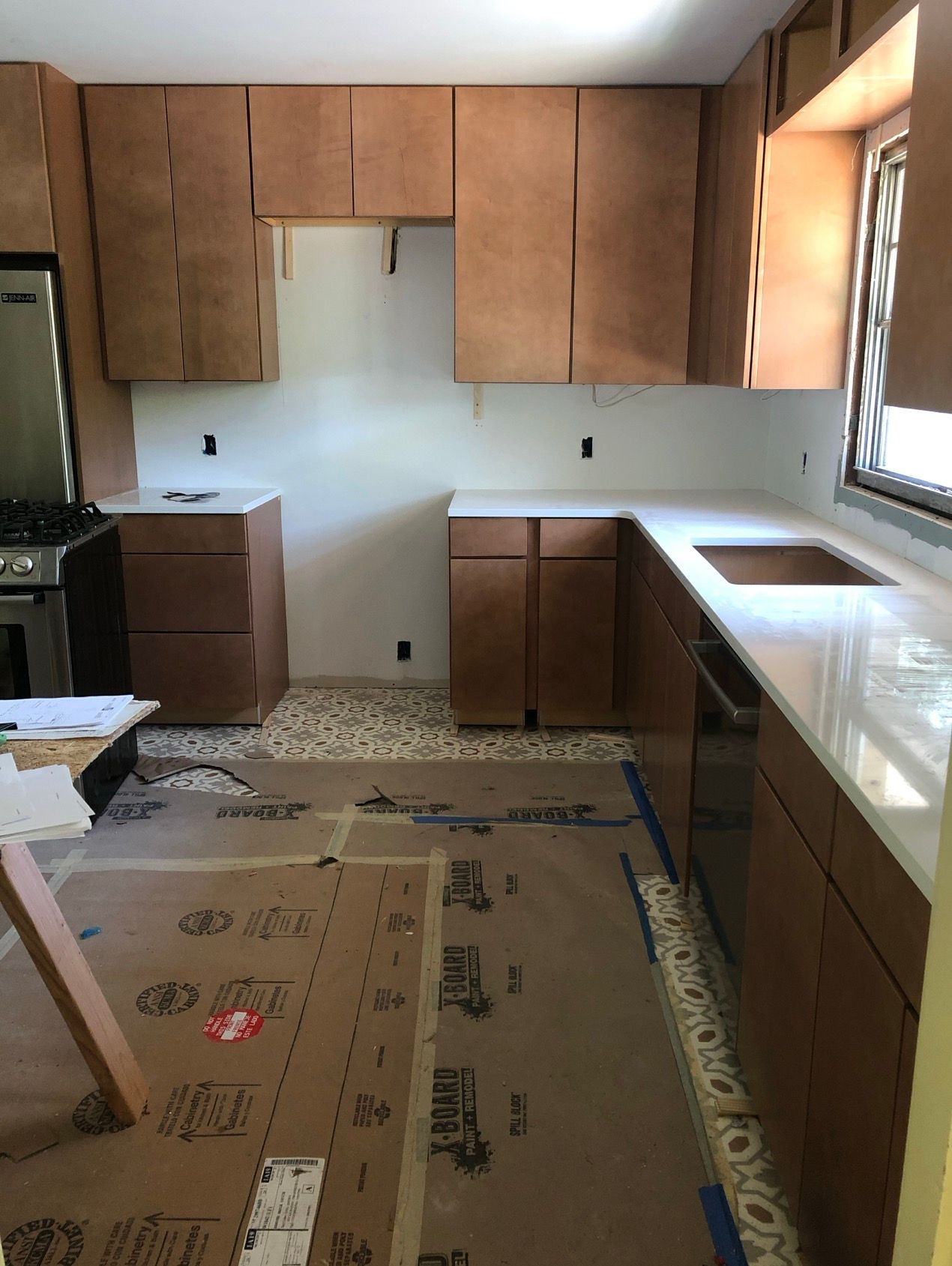 Kitchen under construction with light countertops, brown cabinets, and patterned floor.