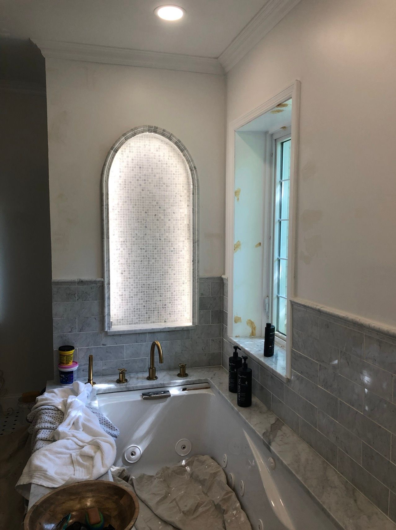 Bathroom with a tub, mosaic tile, arched window niche with frosted glass, and a small window.