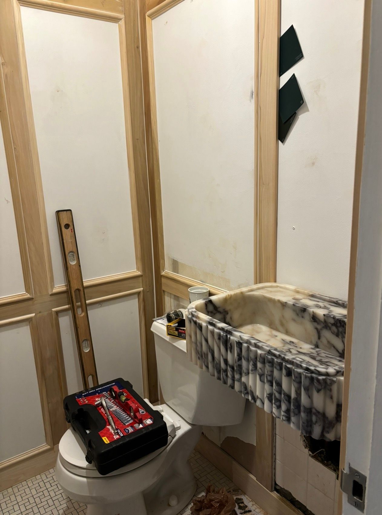 Bathroom remodel in progress with a new marble sink and toilet, framed wall panels, and tools.