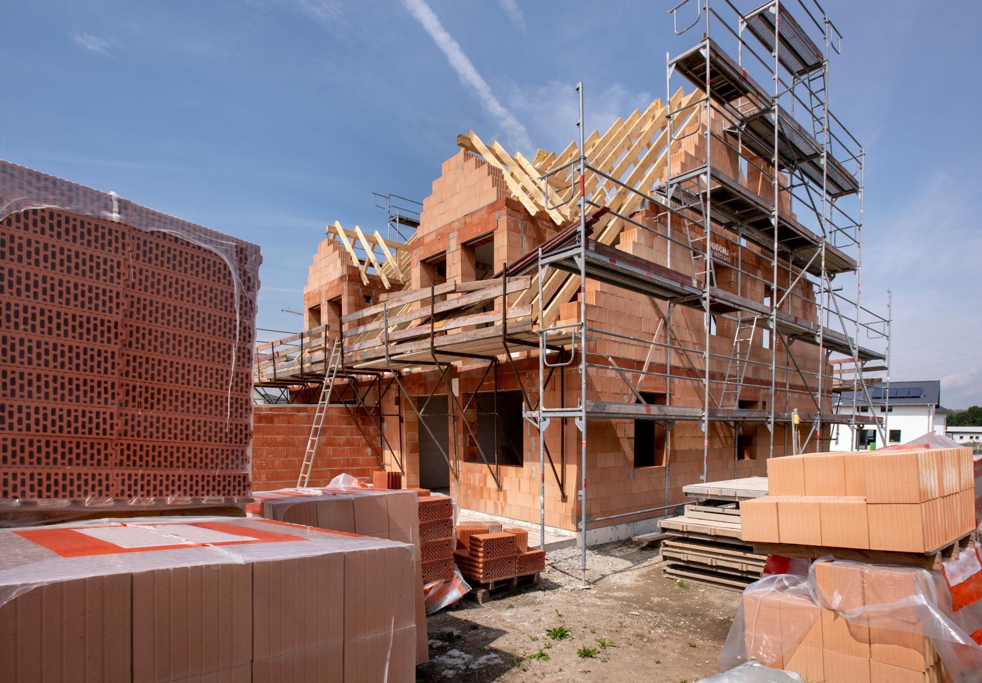 Construction site of a brick house with scaffolding, materials, and a blue sky.