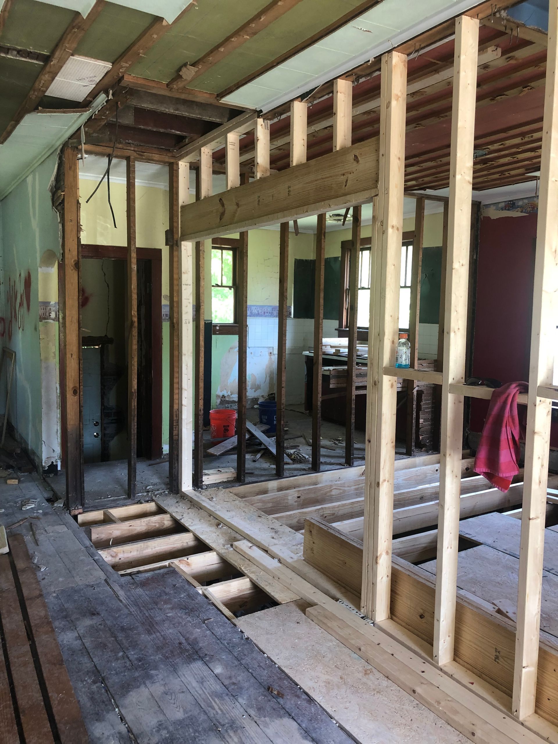 Interior renovation: exposed framing, unfinished walls and floors, doorway to another room.