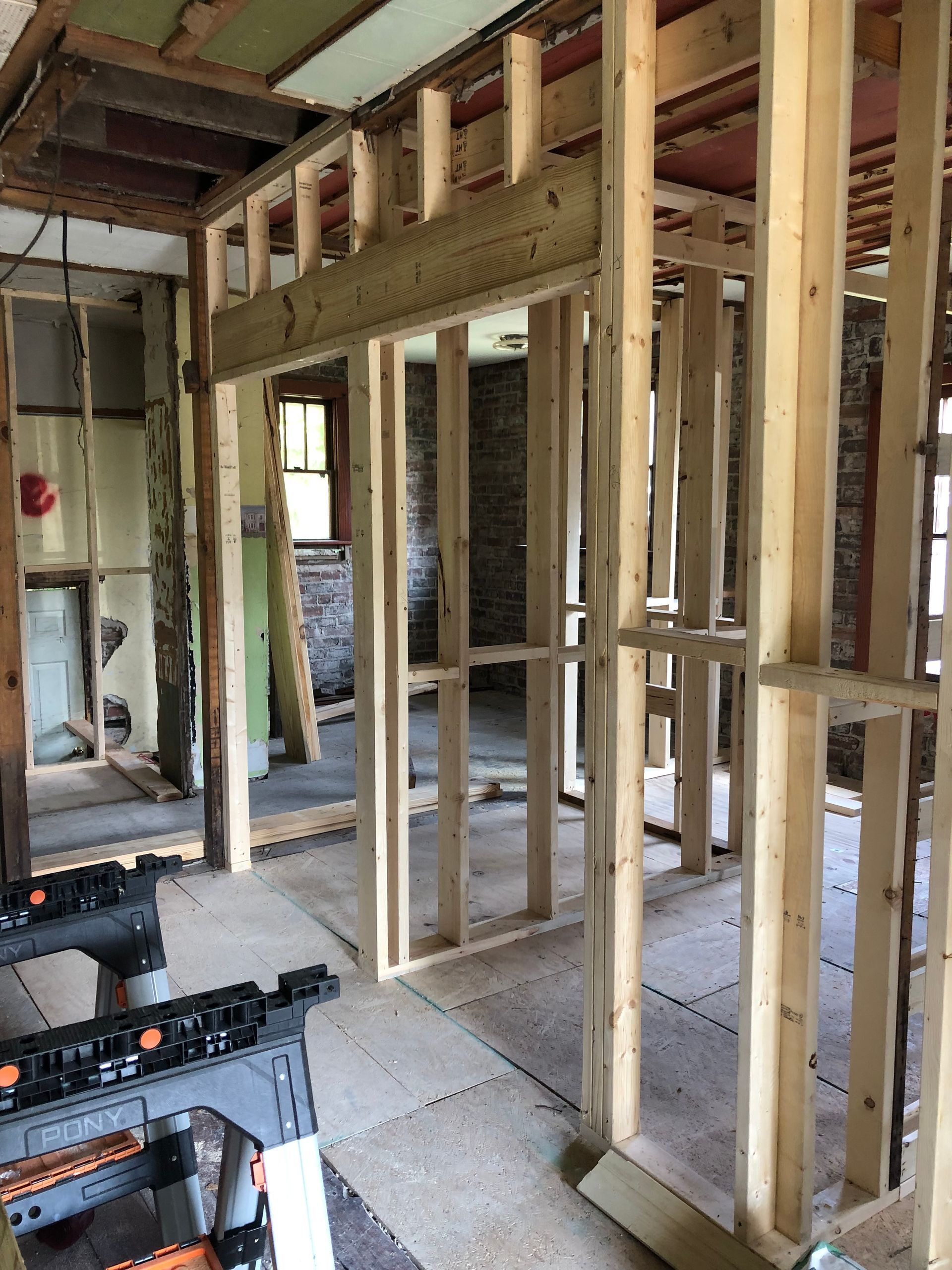 Interior framing of a room during construction. Wooden studs form walls and doorways against existing brick and insulation.