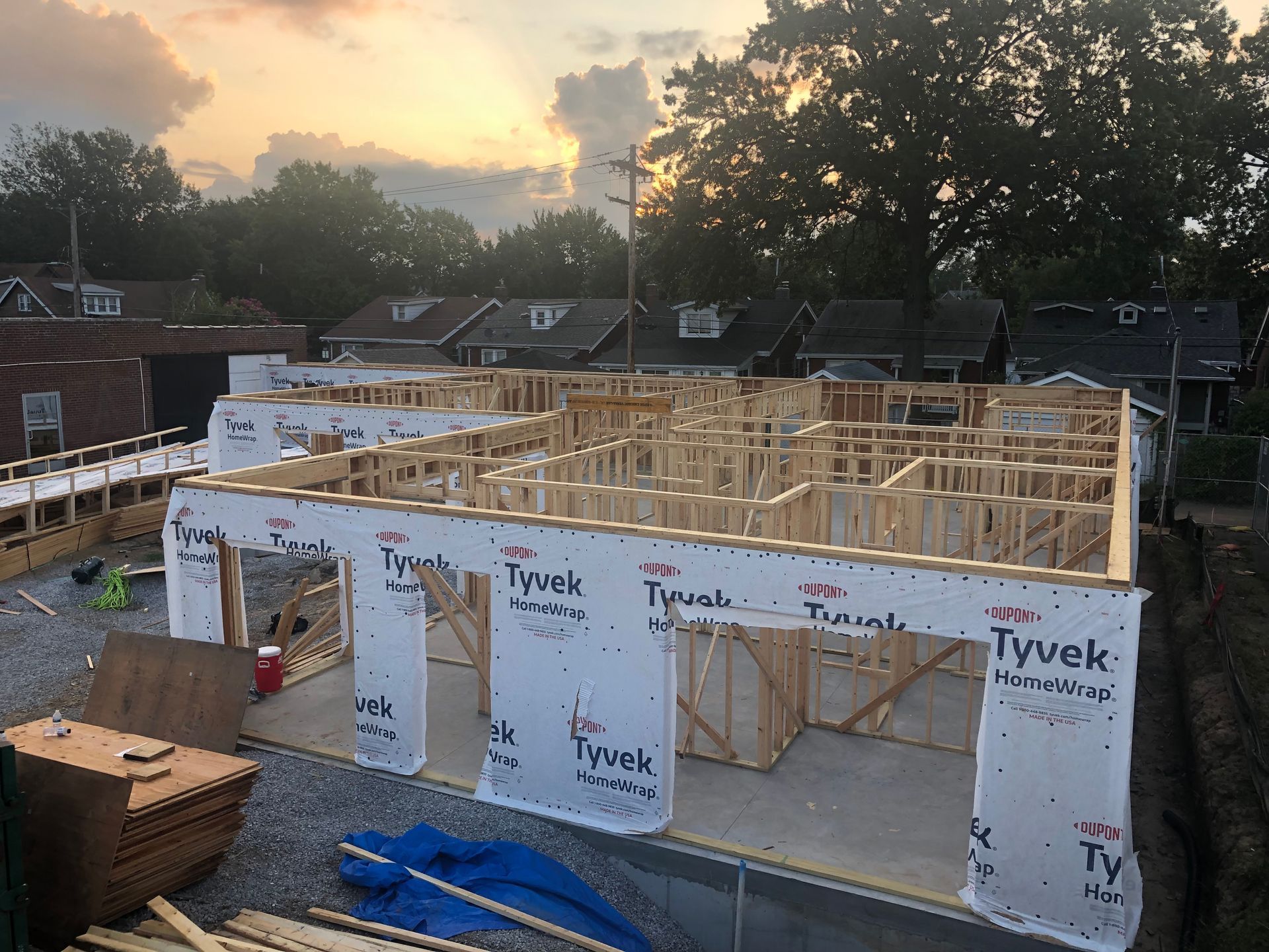 Construction site of a wooden framed building, wrapped in Tyvek, under a sunset sky.