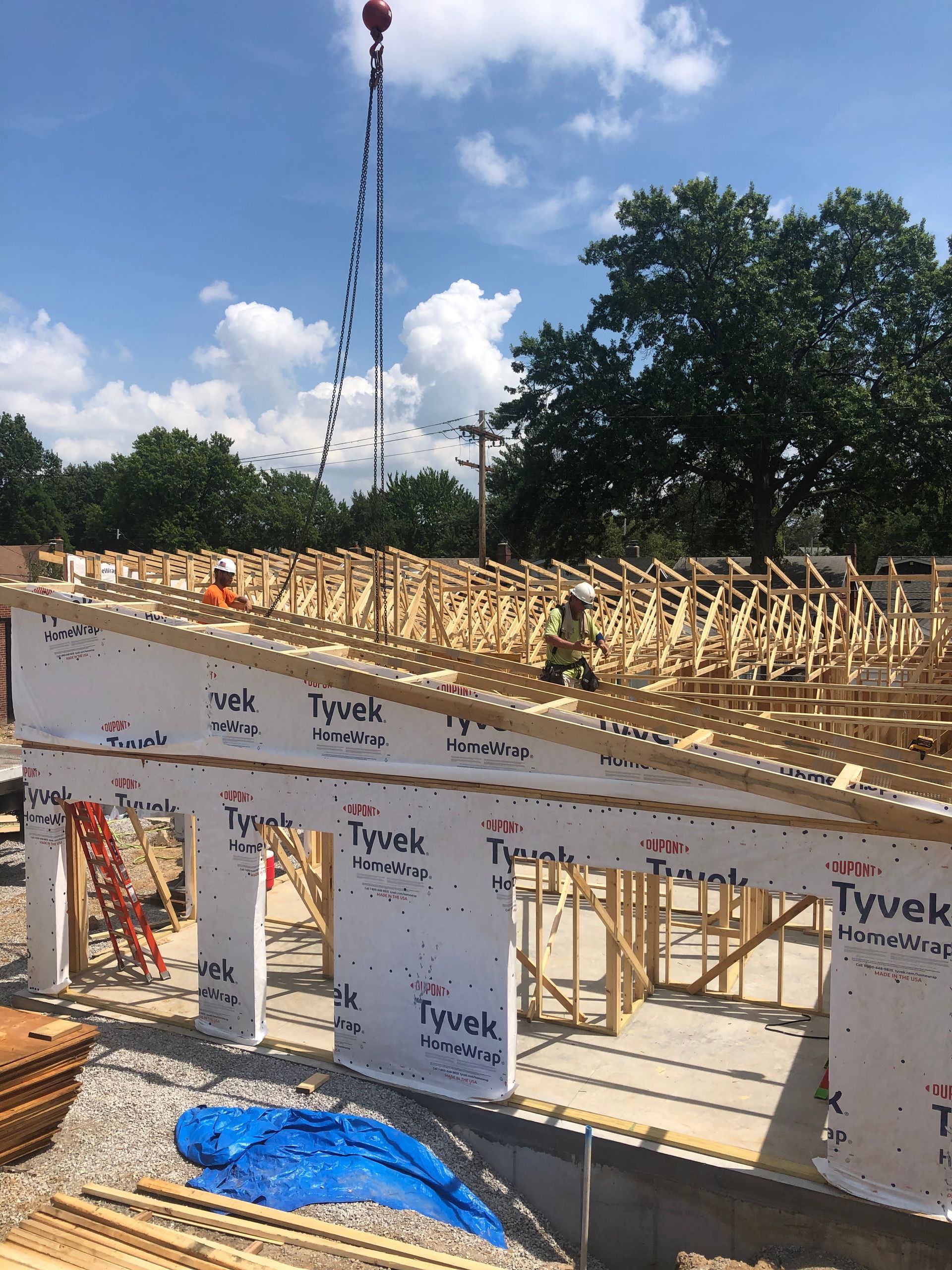 Construction of a building with workers on roof installing trusses, crane overhead; sunny day.