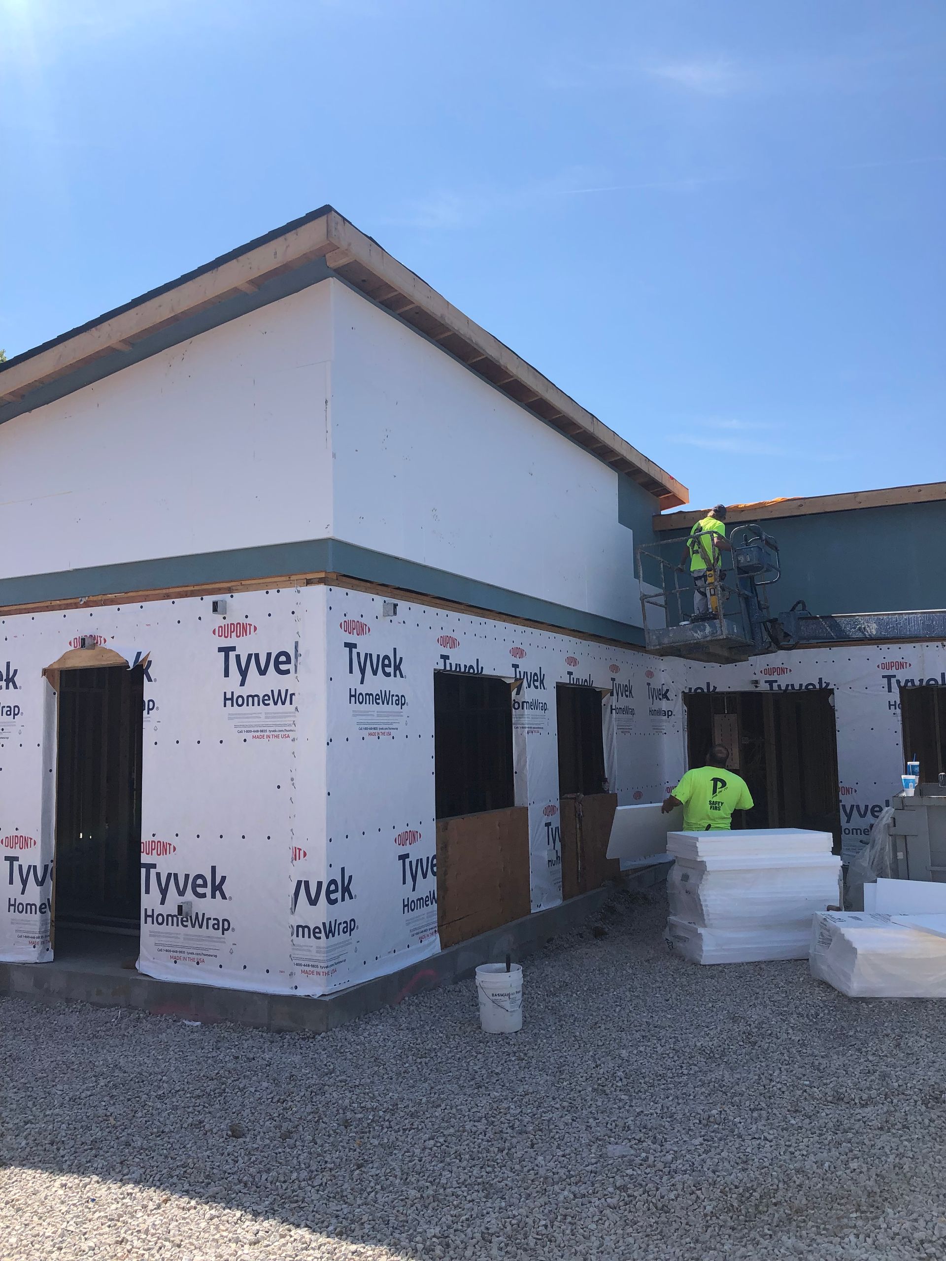 Building under construction; workers installing foam insulation on exterior walls.