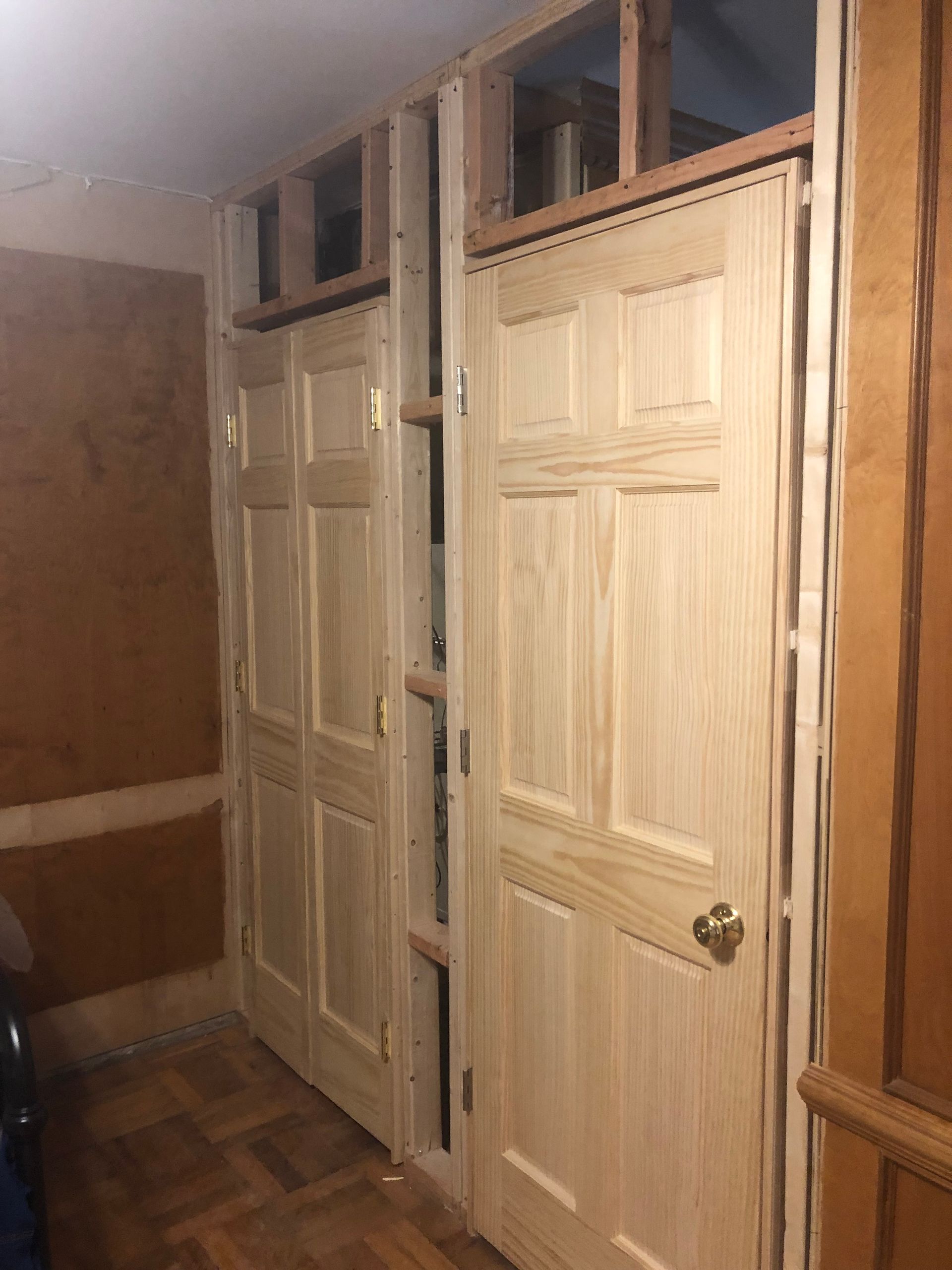 Two light wood doors in a partially framed wall. One door has a knob. Wooden framework is visible.