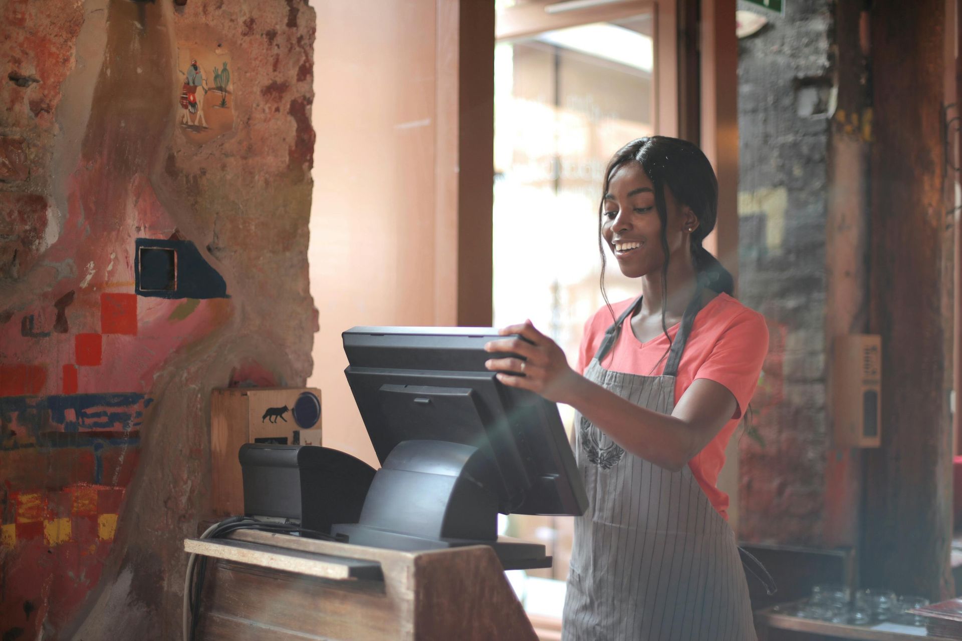 Person in apron smiles, operates a POS system behind a restaurant counter.