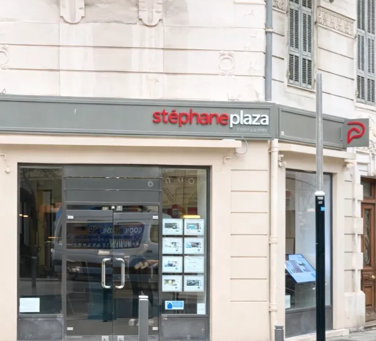 Une vitrine d'angle pour l'agence immobilière Stéphane Plaza, avec une enseigne grise et des annonces immobilières en vitrine.