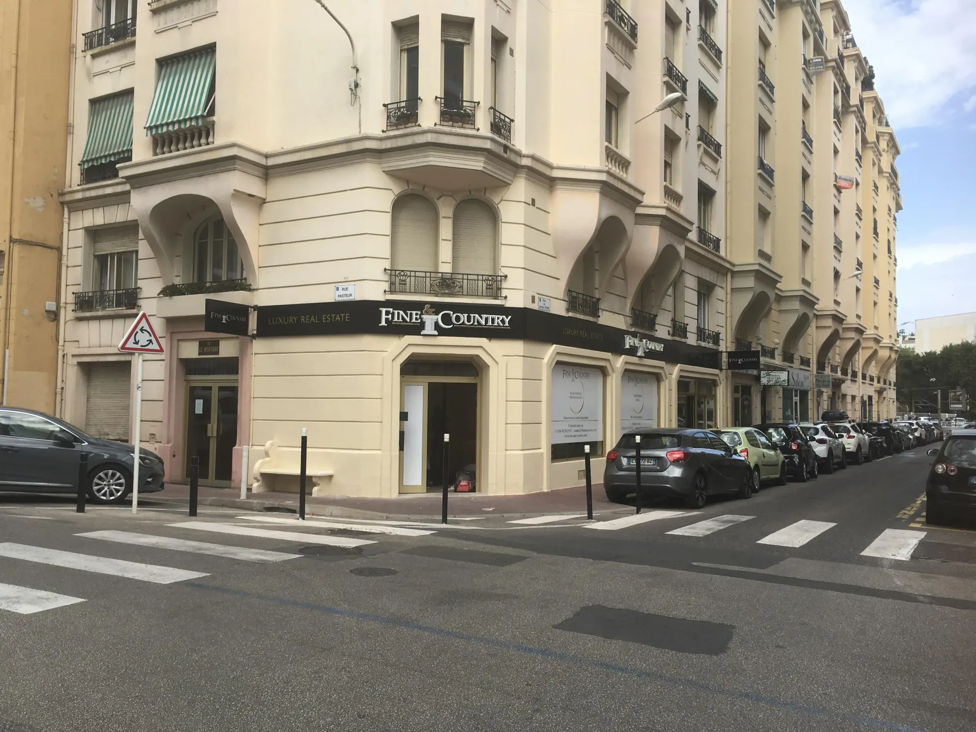 Vue d'angle d'un immeuble d'appartements européen aux couleurs claires, avec un commerce au rez-de-chaussée, par une journée ensoleillée.