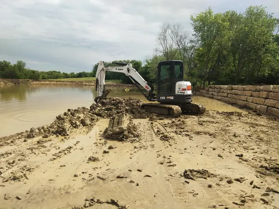 A bobcat excavator is working in the mud near a body of water