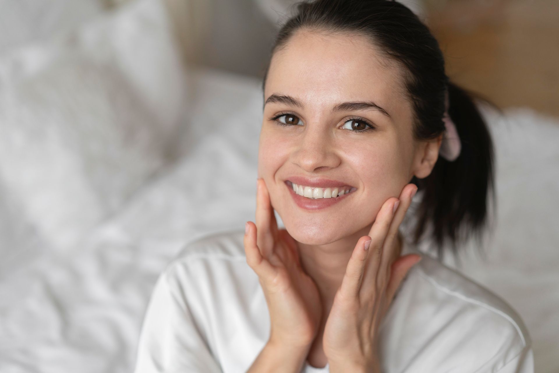 A woman is smiling while touching her face and looking at the camera after facial.