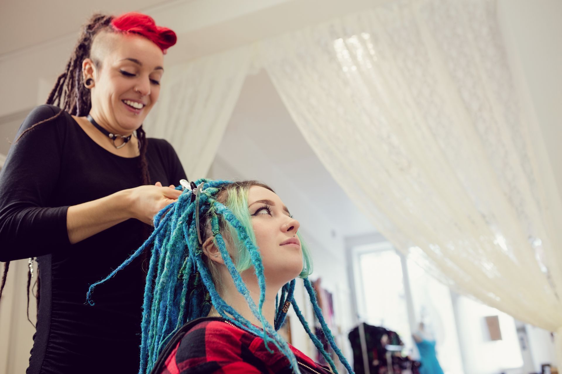 A woman with blue dreadlocks is getting her hair done by a hairdresser.