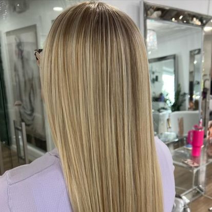 A woman with long blonde hair is sitting in front of a mirror in a salon.