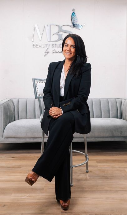 A woman in a suit is sitting on a chair in front of a couch.