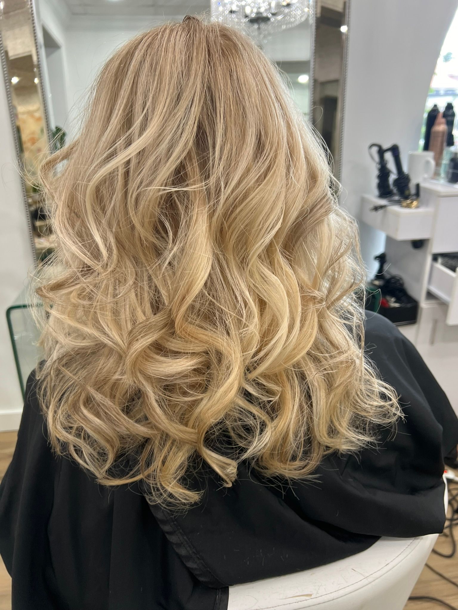 A woman with blonde curly hair is sitting in a chair in a salon.