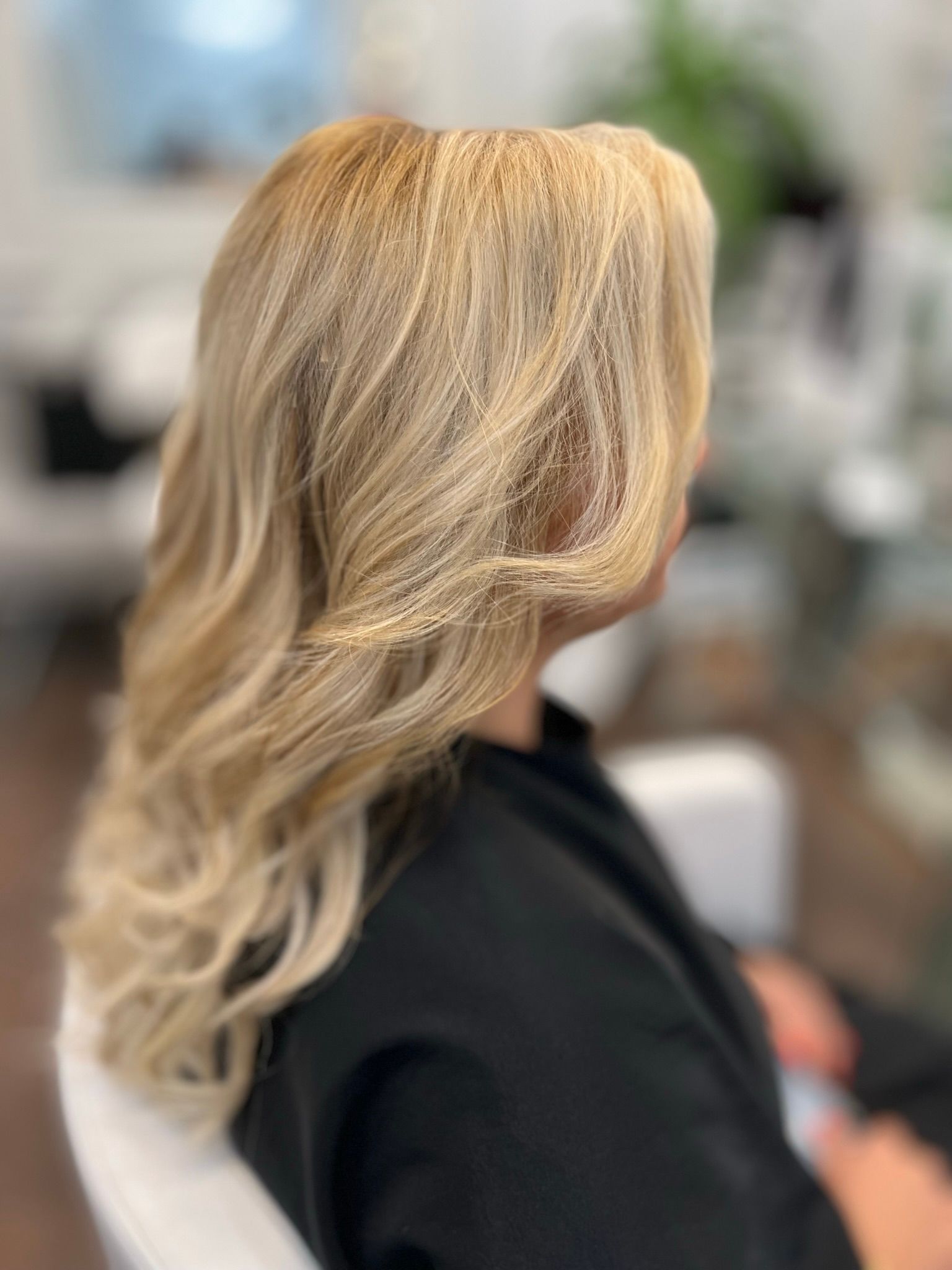 A woman with long blonde hair is sitting in a chair in a salon.
