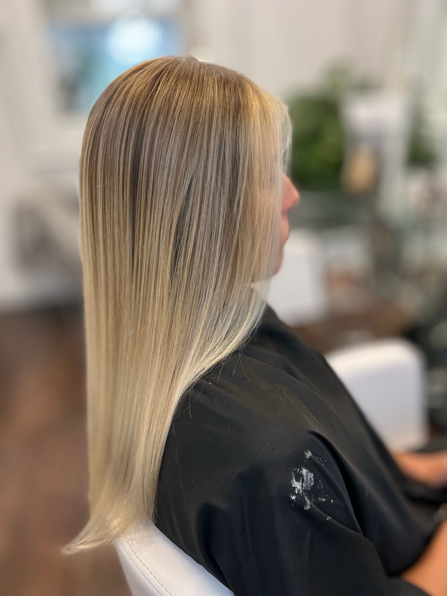 A woman with long blonde hair is sitting in a chair in a salon.