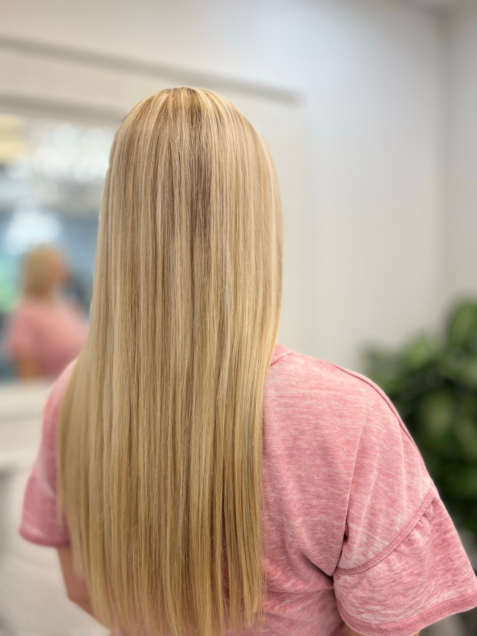 A woman with long blonde hair is wearing a pink shirt.