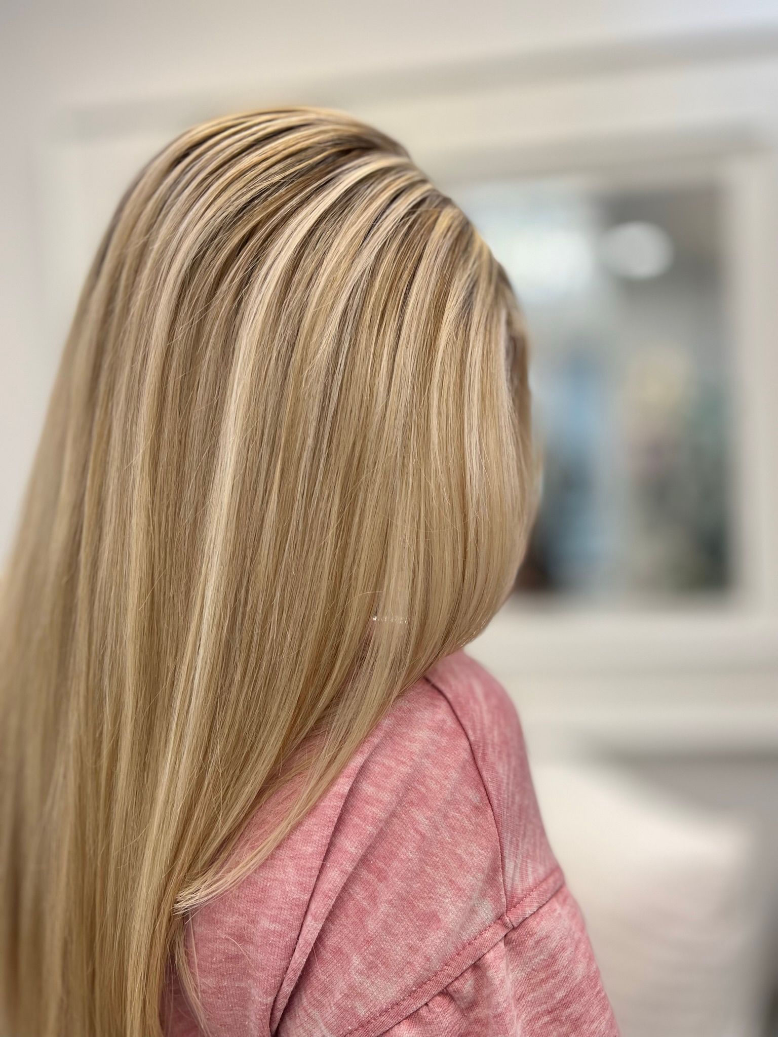 A woman with long blonde hair is wearing a pink sweater.