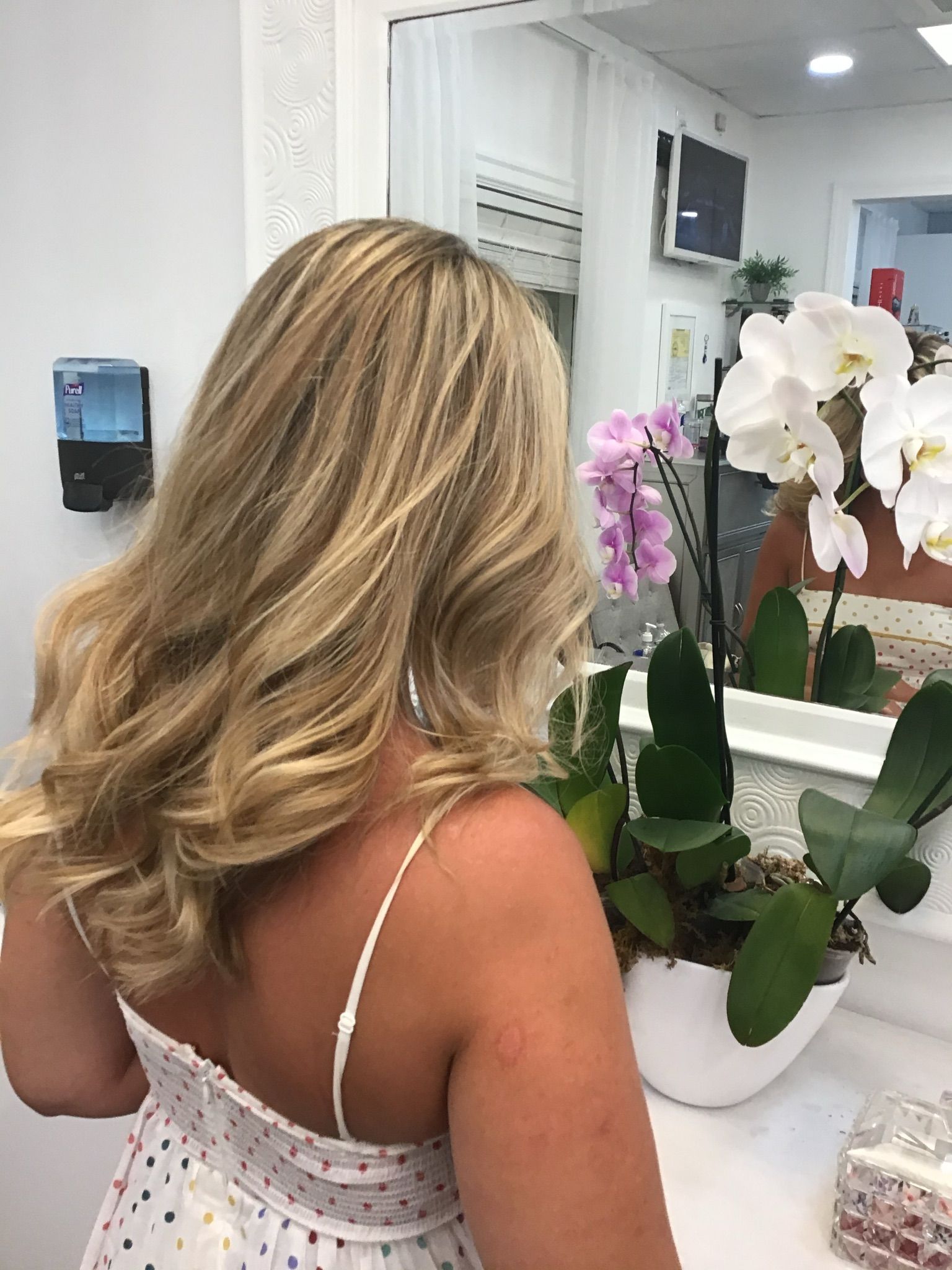 A woman is standing in front of a mirror with flowers in a vase.