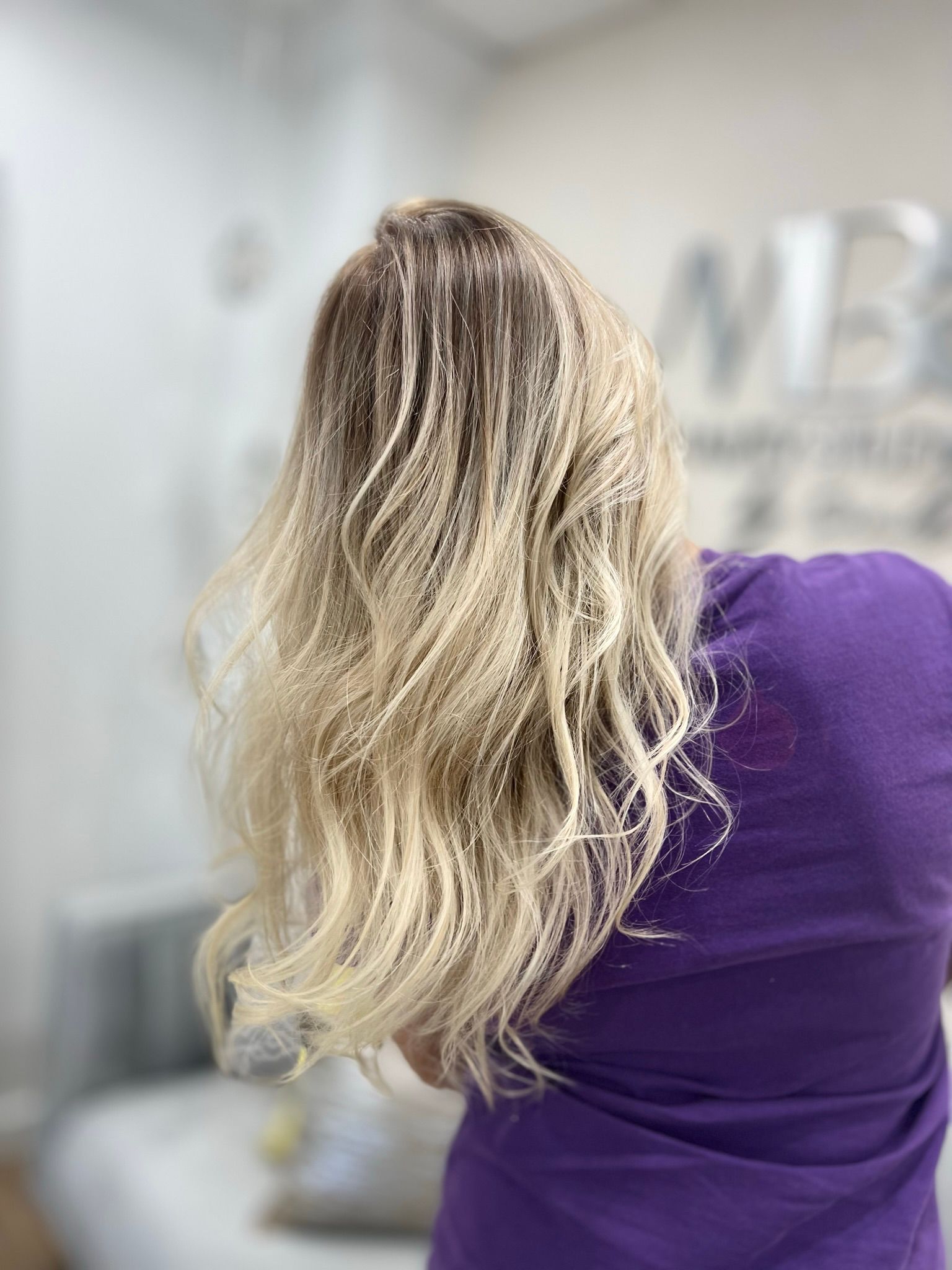 A woman with long blonde hair is wearing a purple shirt.