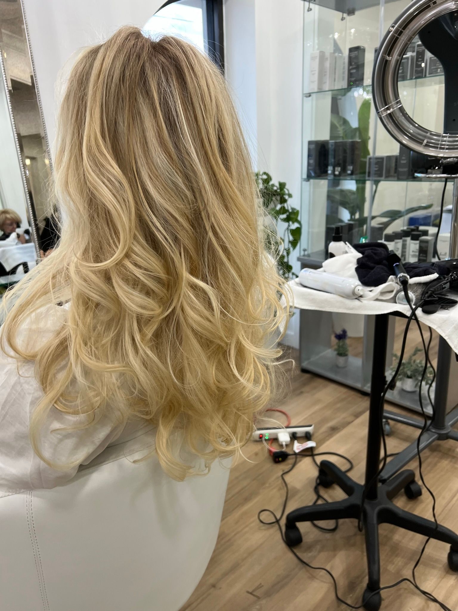 A woman with long blonde hair is sitting in a chair in a salon.