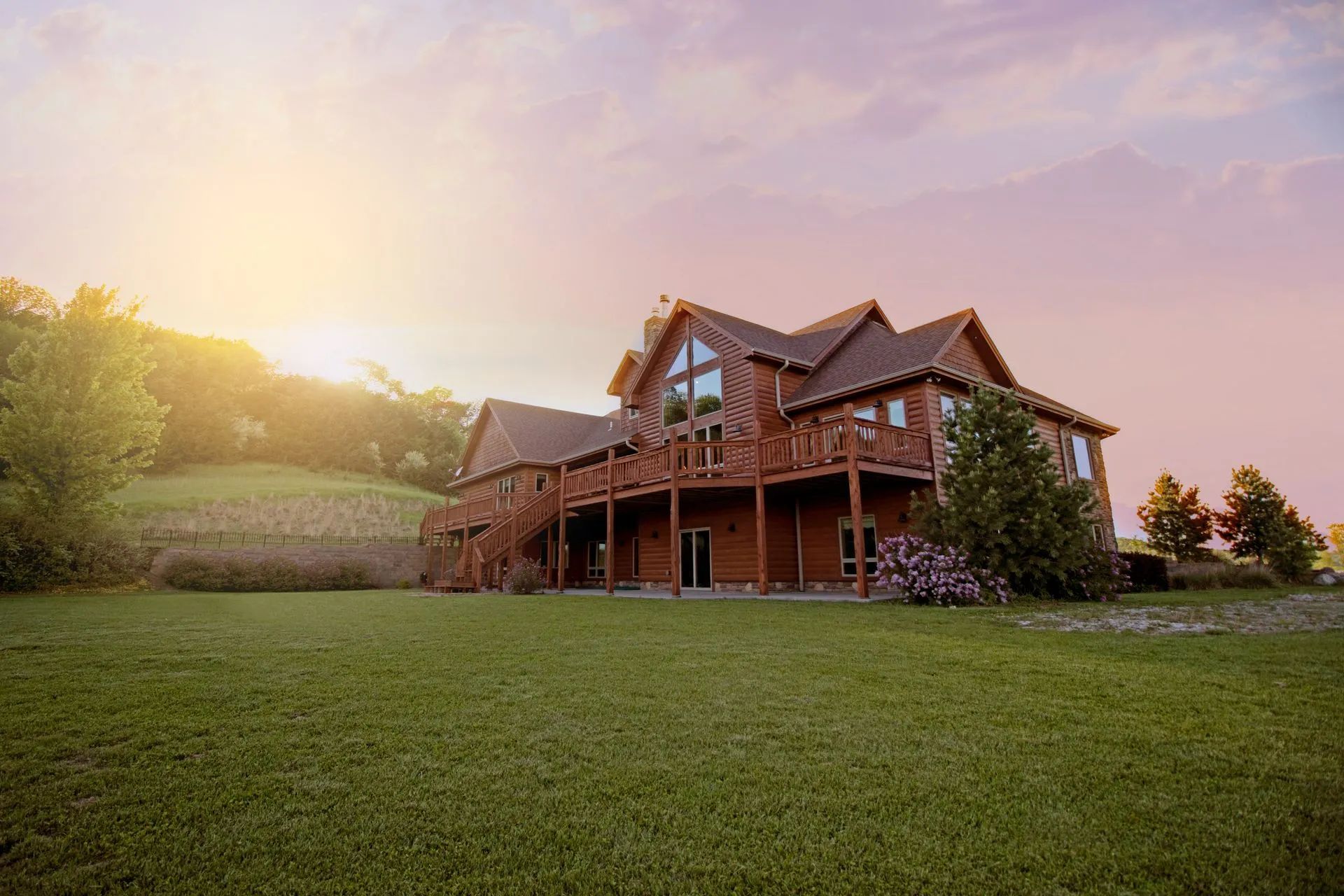 A large log home is sitting on top of a lush green hillside.