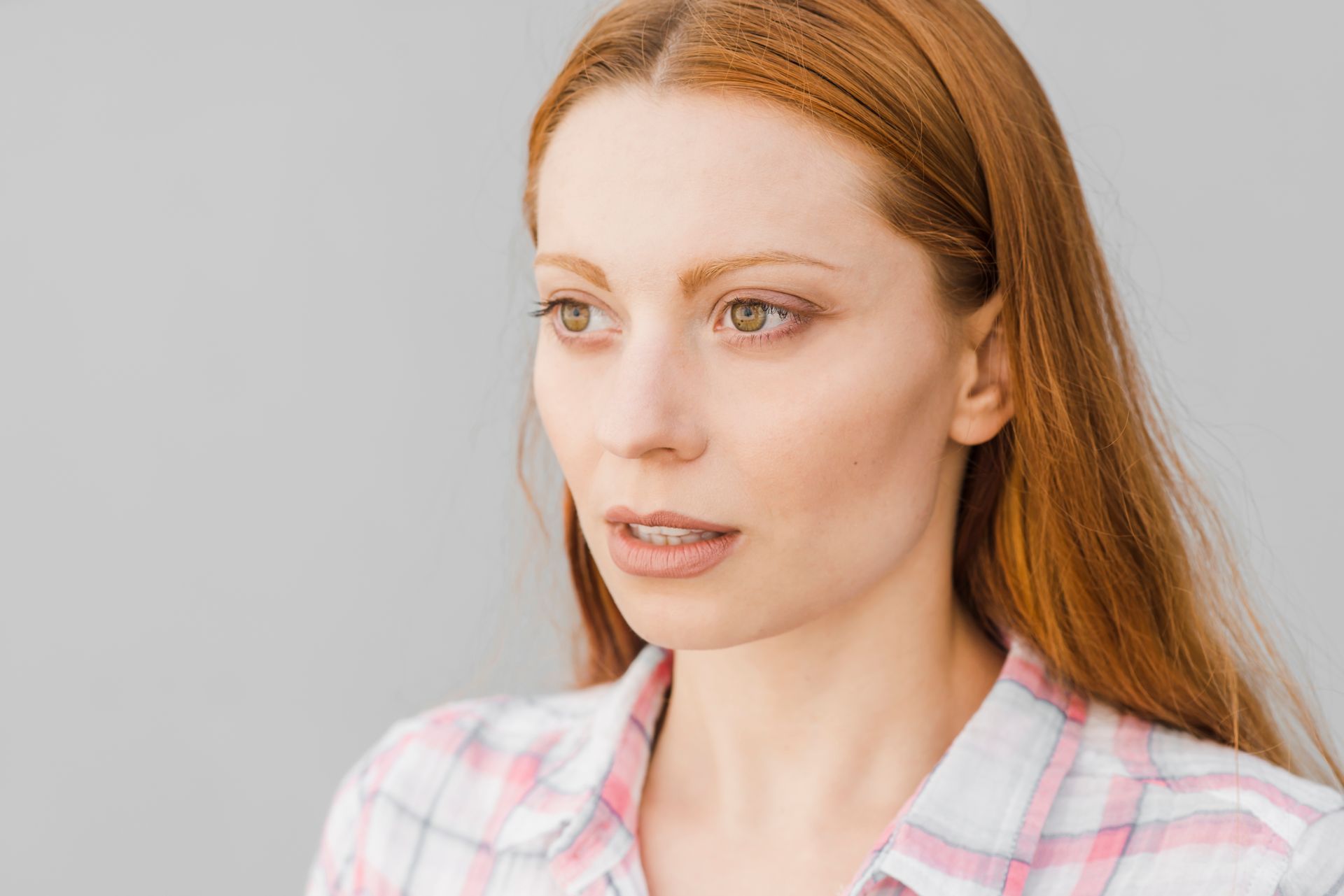 A woman with red hair is wearing a plaid shirt and looking to the side.