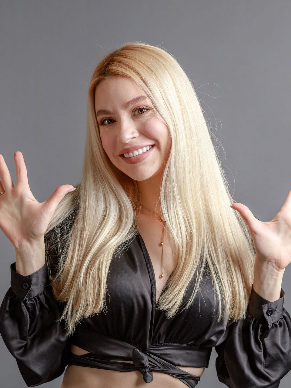 A woman with blonde hair is wearing a black crop top and smiling.