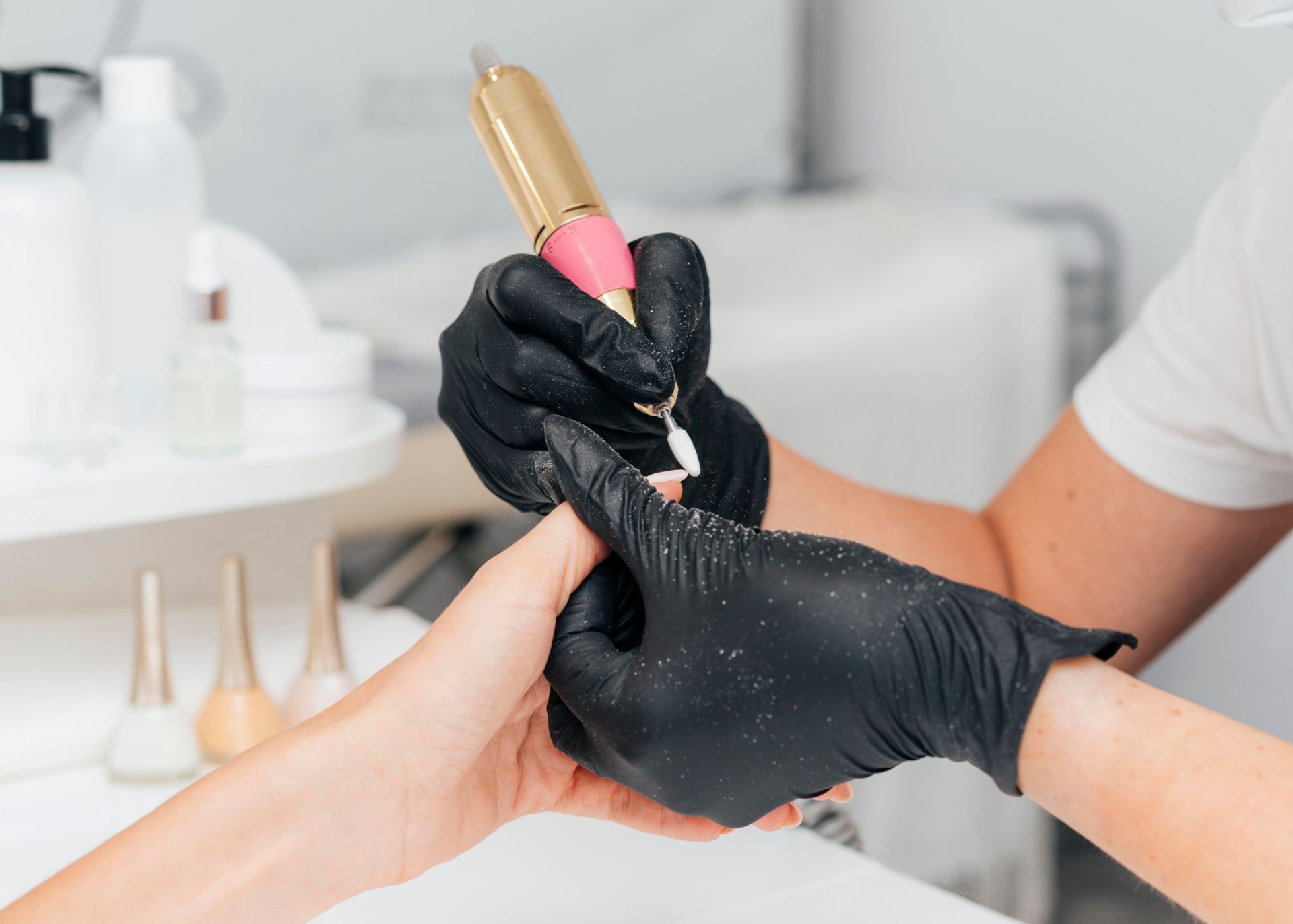 A woman wearing a mask and pink gloves is doing a manicure to a woman.